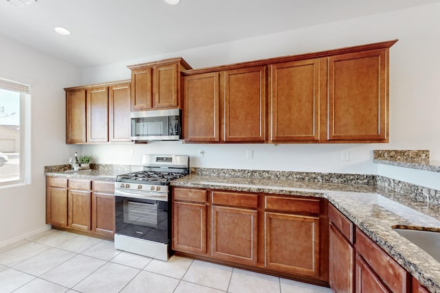 kitchen with light tile patterned floors, brown cabinetry, stone counters, recessed lighting, and stainless steel appliances