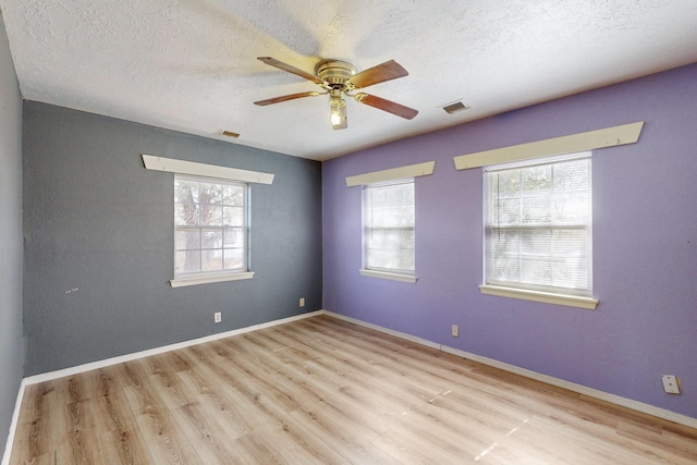 empty room with plenty of natural light, wood finished floors, visible vents, and baseboards