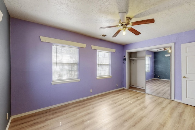 unfurnished bedroom featuring a textured ceiling, ceiling fan, wood finished floors, visible vents, and a closet