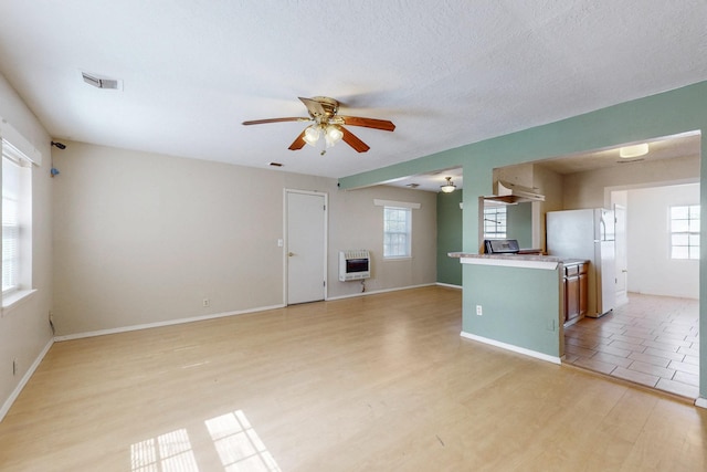 unfurnished living room featuring a textured ceiling, ceiling fan, visible vents, light wood-style floors, and heating unit