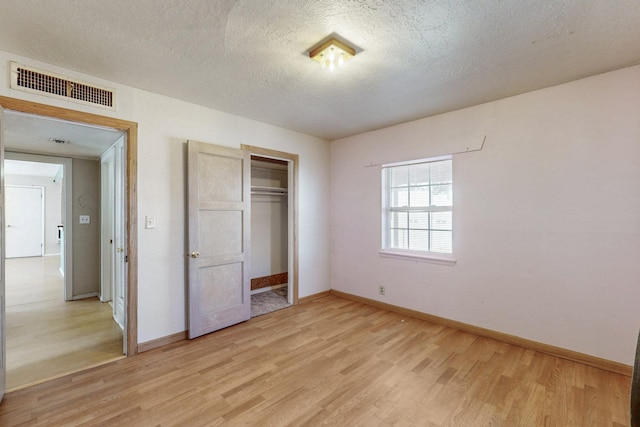 unfurnished bedroom with a closet, visible vents, light wood-style flooring, a textured ceiling, and baseboards