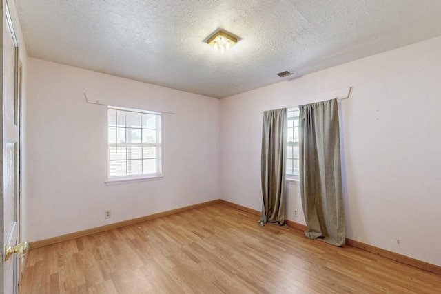 spare room featuring light wood finished floors, baseboards, visible vents, and a textured ceiling