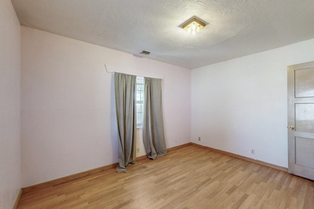 spare room with baseboards, visible vents, light wood-style flooring, and a textured ceiling