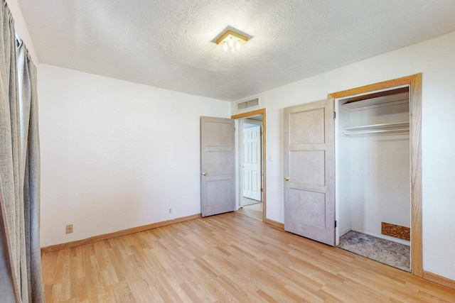 unfurnished bedroom featuring light wood-style floors, visible vents, a textured ceiling, and baseboards