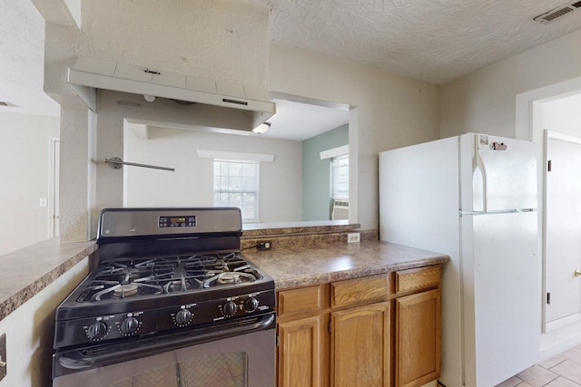 kitchen featuring visible vents, freestanding refrigerator, a textured ceiling, under cabinet range hood, and gas stove