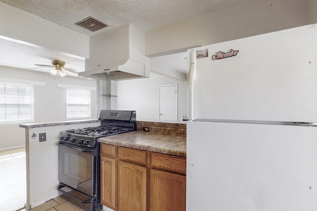 kitchen with visible vents, black gas range oven, ceiling fan, freestanding refrigerator, and a textured ceiling