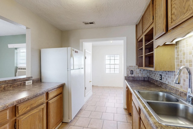 kitchen featuring tasteful backsplash, visible vents, brown cabinetry, freestanding refrigerator, and a sink