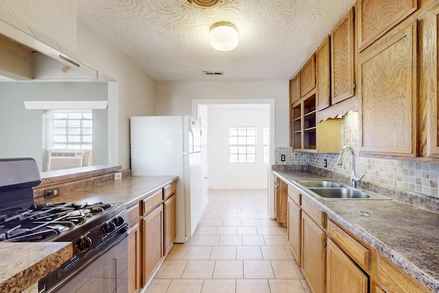 kitchen featuring a sink, visible vents, freestanding refrigerator, decorative backsplash, and stainless steel range with gas stovetop