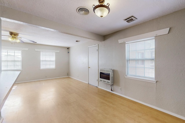 spare room with baseboards, visible vents, heating unit, and wood finished floors