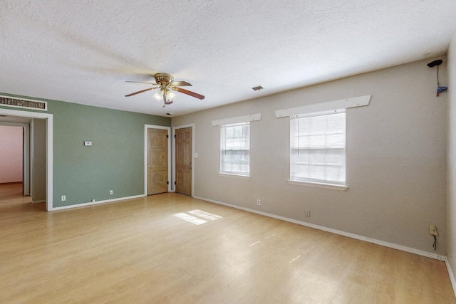 empty room with light wood-style floors, a ceiling fan, visible vents, and a textured ceiling