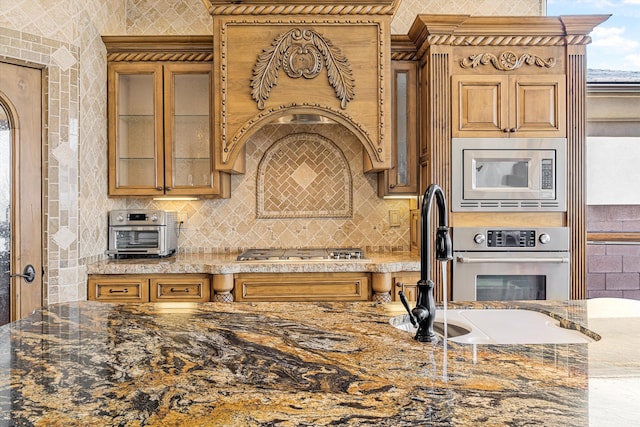 kitchen featuring stone counters, stainless steel appliances, a sink, tasteful backsplash, and glass insert cabinets