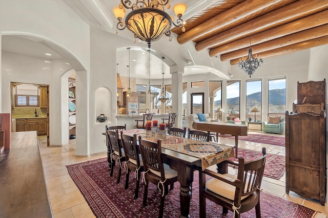 dining room featuring arched walkways, a notable chandelier, a towering ceiling, a mountain view, and beamed ceiling