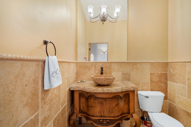 bathroom featuring toilet, a wainscoted wall, vanity, tile walls, and an inviting chandelier