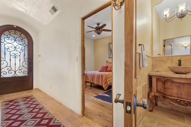 entrance foyer with ceiling fan with notable chandelier, visible vents, and stone tile floors