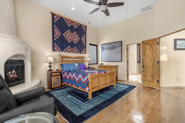 bedroom with a fireplace, visible vents, a towering ceiling, a ceiling fan, and hardwood / wood-style floors