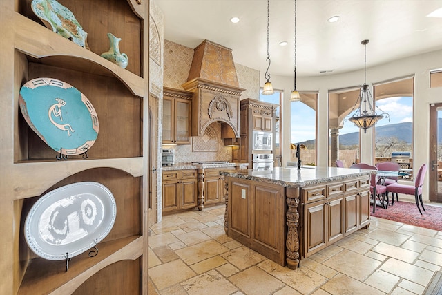 kitchen with light stone counters, stainless steel appliances, stone tile flooring, brown cabinets, and decorative light fixtures