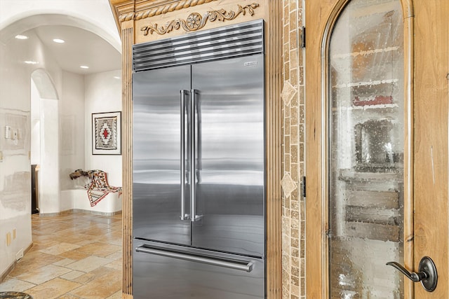 kitchen featuring arched walkways, stone tile floors, recessed lighting, and stainless steel built in fridge