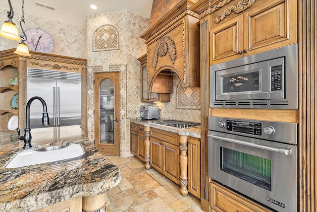 kitchen featuring visible vents, brown cabinetry, built in appliances, stone tile flooring, and a sink