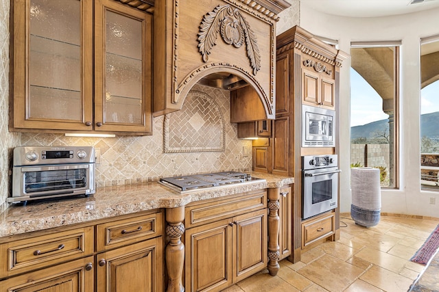 kitchen featuring glass insert cabinets, stainless steel appliances, stone tile flooring, light countertops, and backsplash