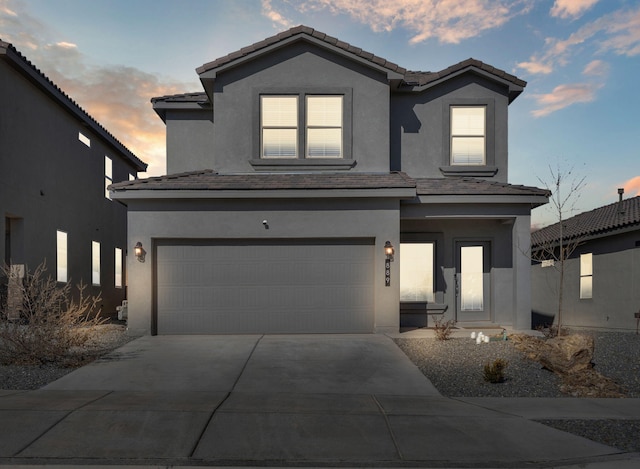 traditional home featuring a tiled roof, an attached garage, driveway, and stucco siding