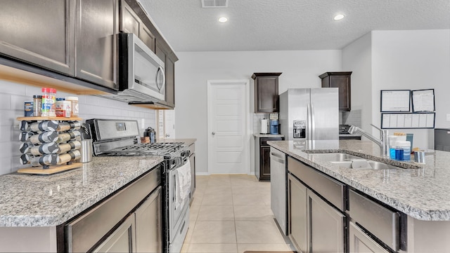 kitchen with light stone countertops, an island with sink, light tile patterned floors, stainless steel appliances, and a sink