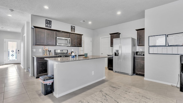 kitchen featuring visible vents, a center island with sink, backsplash, stainless steel appliances, and dark brown cabinets