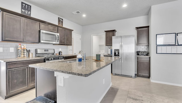 kitchen with visible vents, an island with sink, a sink, dark brown cabinetry, and appliances with stainless steel finishes