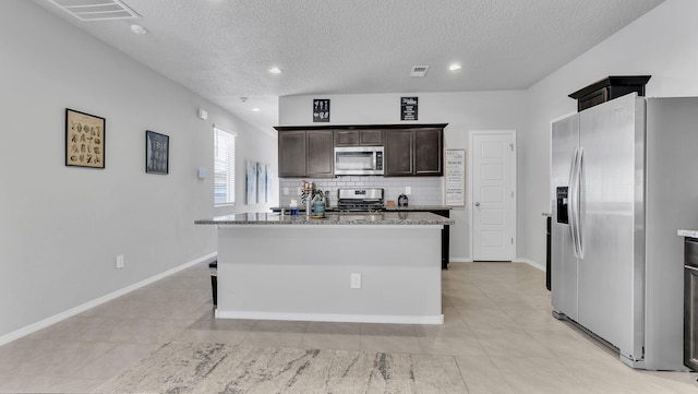 kitchen with tasteful backsplash, visible vents, dark brown cabinetry, appliances with stainless steel finishes, and stone countertops