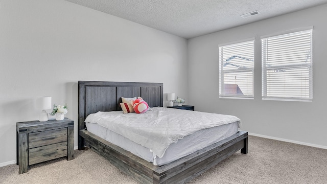 bedroom with baseboards, light carpet, a textured ceiling, and visible vents