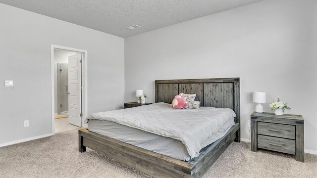 carpeted bedroom featuring visible vents, baseboards, a textured ceiling, and ensuite bath