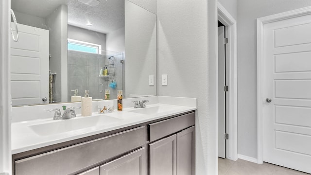 bathroom with a textured ceiling, tile patterned floors, tiled shower, and a sink