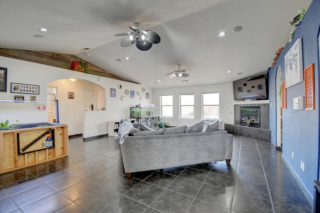 living room featuring arched walkways, a ceiling fan, vaulted ceiling, dark tile patterned flooring, and a tile fireplace