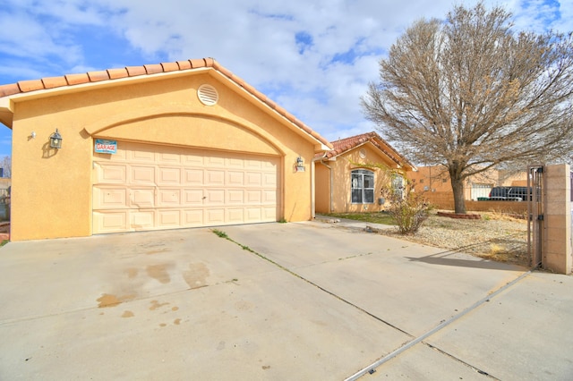 mediterranean / spanish house featuring an attached garage, fence, a tiled roof, concrete driveway, and stucco siding