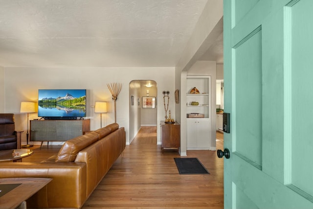 living room featuring arched walkways, built in shelves, a textured ceiling, and light wood-type flooring