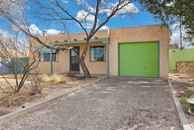 pueblo revival-style home featuring gravel driveway, a chimney, stucco siding, an attached garage, and fence