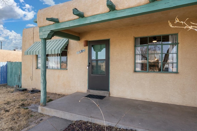 view of exterior entry with a patio, fence, and stucco siding