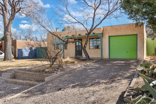 pueblo revival-style home with gravel driveway, a chimney, an attached garage, and stucco siding