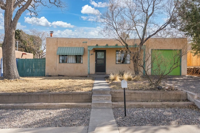 pueblo revival-style home featuring an attached garage, fence, and stucco siding