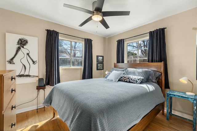 bedroom featuring multiple windows, ceiling fan, baseboards, and wood finished floors