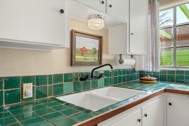 kitchen with tile counters, white cabinets, and a sink