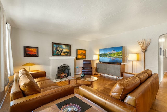 living room featuring a fireplace with flush hearth, arched walkways, and wood finished floors