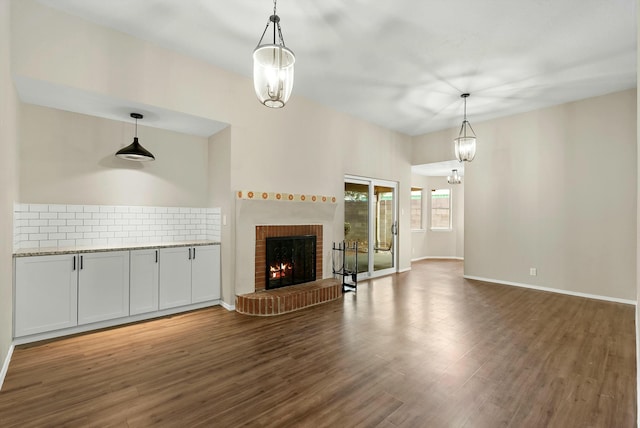 unfurnished living room with a chandelier, a brick fireplace, baseboards, and wood finished floors