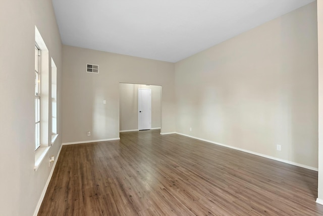 empty room with wood finished floors, visible vents, and baseboards