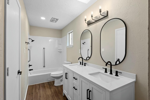 full bath with toilet, a textured ceiling, a sink, and wood finished floors