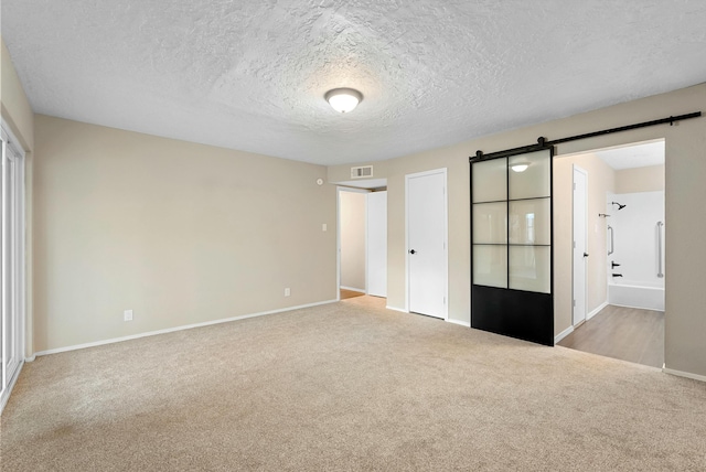 unfurnished bedroom with a textured ceiling, a barn door, visible vents, baseboards, and carpet