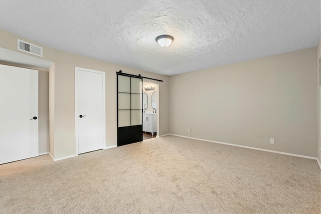 unfurnished bedroom featuring carpet floors, visible vents, a barn door, a textured ceiling, and baseboards