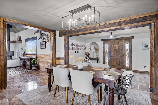 dining area featuring beamed ceiling, wainscoting, a wood stove, and an inviting chandelier