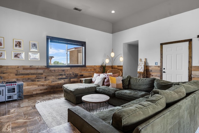 living area with visible vents, wooden walls, a wainscoted wall, recessed lighting, and stone finish floor