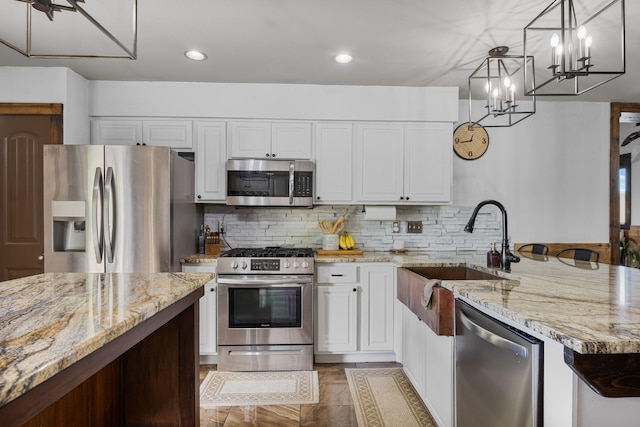 kitchen with a sink, light stone counters, appliances with stainless steel finishes, and white cabinetry