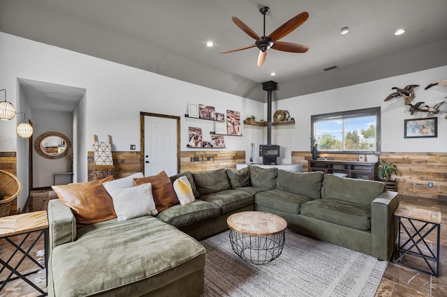 living room featuring wooden walls, visible vents, a wood stove, and ceiling fan